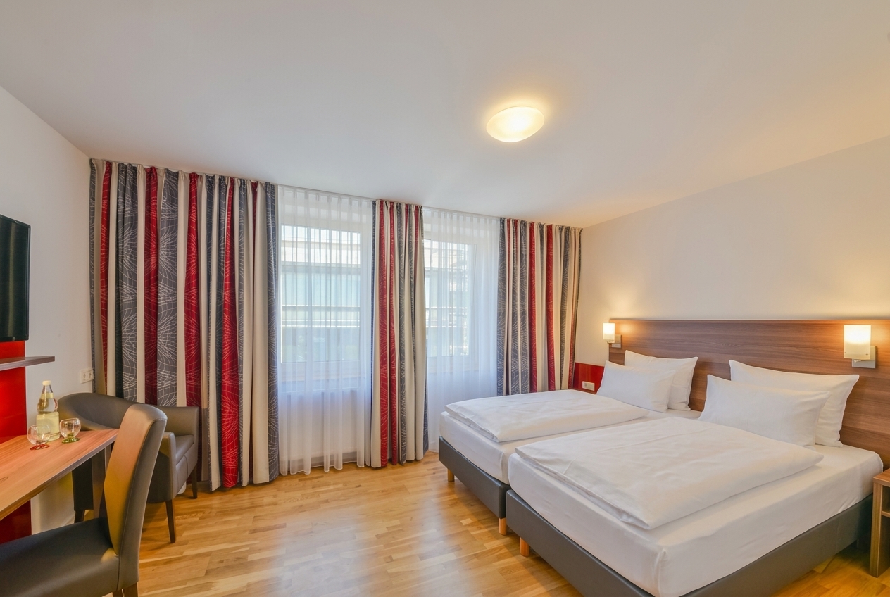 Doppelzimmer mit großem Doppelbett, Nachttischen und hellen Fenstern